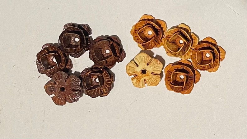 May include: Two sets of six decorative flower-shaped metal embellishments. One set is brown and the other is light brown.