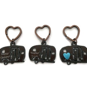May include: Three brown metal camper keychains with heart-shaped key rings. One keychain says "Happy Camper", another says "Trailer Trash", and the third has a blue heart accent.