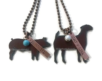 May include: Two necklaces featuring animal silhouettes, a pig and a goat, with a charm that reads "Pig Girl" and "Goat Girl".
