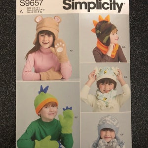 Könnte beinhalten: Simplicity Schnittmuster S9657 mit Kinderhüten und -fäustlingen. Das Muster enthält Designs für einen Bärenhut und -fäustlinge, einen Dinosaurierhut und -schal, einen Hut und Schal mit Bienenmotiv sowie einen Schneeflockenhut und -fäustlinge. Das Muster ist einfach zu nähen.