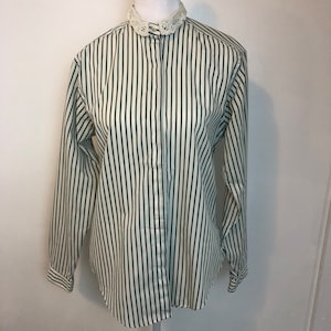 Puede incluir: Una camisa de manga larga a rayas blancas y negras con un cuello de encaje blanco.