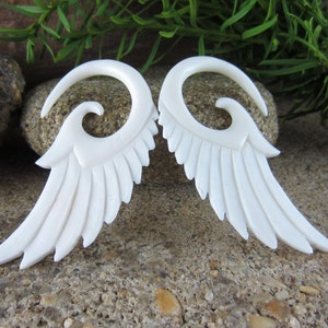 May include: A pair of white bone earrings with a wing design and a spiral detail. The earrings are made of natural bone and have a polished finish.
