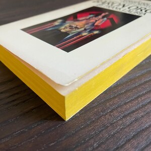 Pu&ograve; includere: Un libro tascabile giallo e bianco con il titolo "The Iron Organ" sulla copertina. La copertina presenta un'illustrazione rossa e nera di una persona che tiene un'arma.