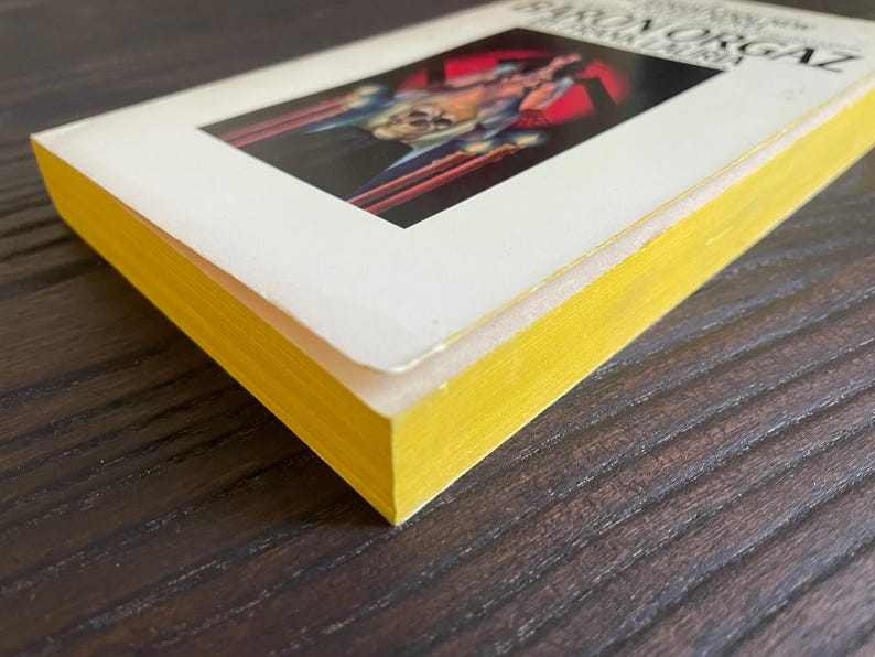 Pu&ograve; includere: Un libro tascabile giallo e bianco con il titolo "The Iron Organ" sulla copertina. La copertina presenta un'illustrazione rossa e nera di una persona che tiene un'arma.