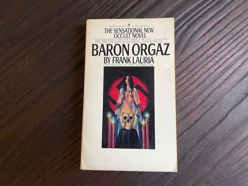 Pu&ograve; includere: Una copertina di un libro tascabile con sfondo bianco e testo nero. Il titolo &egrave; "Baron Orgaz" di Frank Lauria. La copertina presenta una donna con un vestito bianco in piedi di fronte a una svastica rossa con candele e un teschio.
