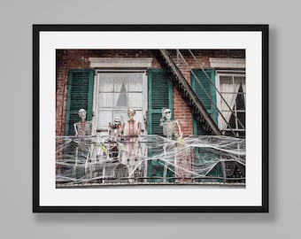 Puede incluir: Fotografía enmarcada de una escena de balcón con temática de Halloween. Hay esqueletos en el balcón, decorados con telarañas y adornos festivos. El edificio tiene contraventanas verdes y una escalera de incendios.