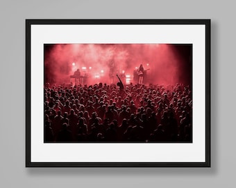 Puede incluir: Una fotografía en blanco y negro enmarcada de un concierto con una luz roja y una multitud de personas en primer plano.