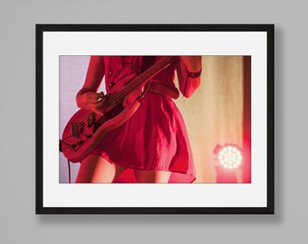 Puede incluir: Una mujer con un vestido rojo toca la guitarra en un escenario. El escenario está iluminado con focos.