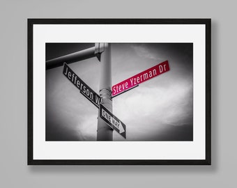 Puede incluir: Fotografía en blanco y negro de una señal de calle con el texto "Steve Yzerman Dr" en letras rojas y "Jefferson W" en letras negras. La señal está montada en un poste con una señal de "Sentido único" debajo.