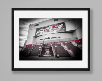 Puede incluir: Una fotografía enmarcada en blanco y negro de Joe Louis Arena con detalles en rojo en las escaleras y la señalización. La impresión se exhibe sobre una mesa consola de metal negro con un reloj de arena de cristal y un objeto rosa pálido.