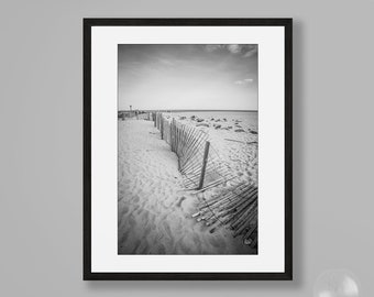 Puede incluir: Fotografía en blanco y negro de una valla de madera en una playa de arena. La valla está parcialmente enterrada en la arena y se extiende hacia la distancia.