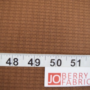May include: Close-up of a brown fabric with a subtle grid pattern. A white measuring tape with black numbers reads 47 to 55 inches.