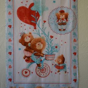 May include: A white fabric panel with a blue border featuring a repeating pattern of hearts. The center of the panel features a whimsical illustration of bears riding a tricycle, holding flowers, and reading books. The fabric is printed with the text "100% cotton print www.studioe.factory.com Paris 2019."
