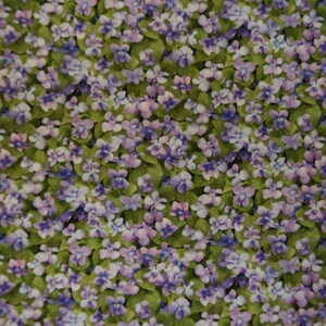 May include: A close-up of a fabric with a repeating pattern of purple and white flowers on a green background.