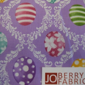 May include: Purple fabric with a white damask pattern and colorful Easter egg designs. The eggs feature various patterns, including stripes, polka dots, and floral designs.