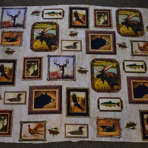 May include: A beige fabric with a repeating pattern of framed images of animals and fish. The frames are brown with a rustic wood grain texture. The images include a moose, deer, bear, fish, birds, and a pheasant.