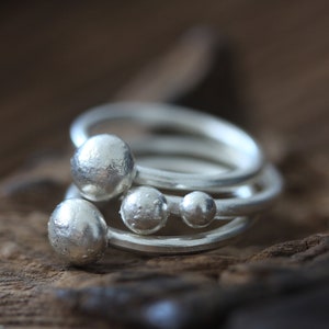 Puede incluir: Un conjunto de cuatro anillos de plata con bolas redondas texturizadas. Los anillos están apilados uno encima del otro.
