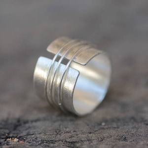 Puede incluir: Un anillo de plata con un diseño geométrico único. El anillo está hecho de múltiples bandas de plata que están entrelazadas.