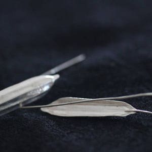 May include: A pair of silver earrings, one shaped like a long, thin pod and the other shaped like a leaf.