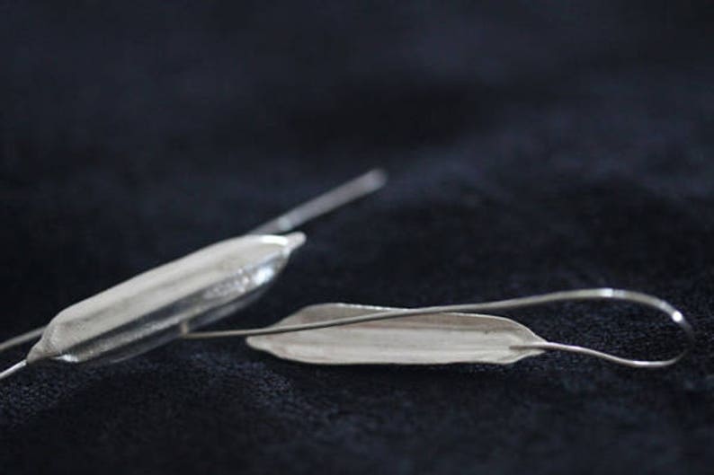 May include: A pair of silver earrings, one shaped like a long, thin pod and the other shaped like a leaf.