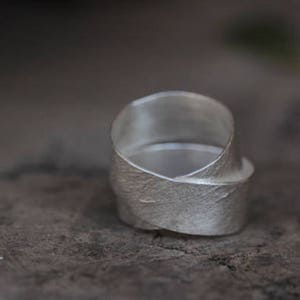 May include: A silver ring with a textured, leaf-like design. The ring is made of a single piece of metal that is twisted and folded to create the design.