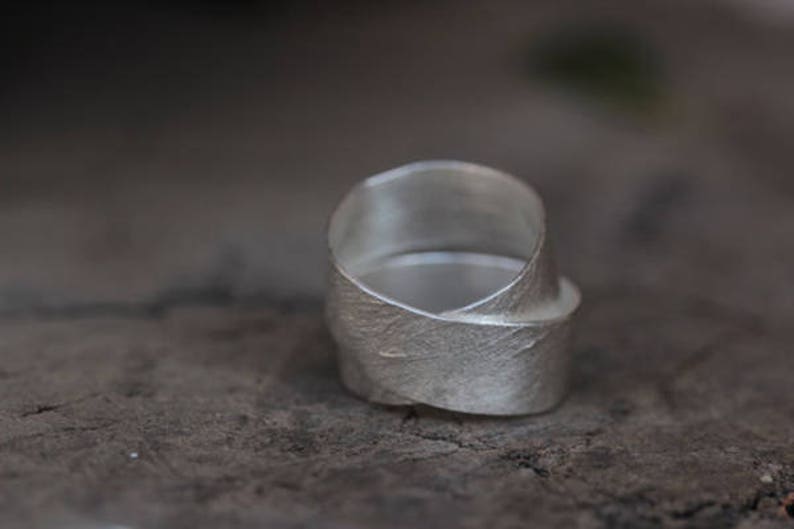 May include: A silver ring with a textured, leaf-like design. The ring is made of a single piece of metal that is twisted and folded to create the design.