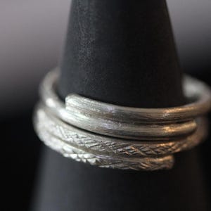May include: Three silver rings stacked on top of each other. The rings are all different widths and have different textures.
