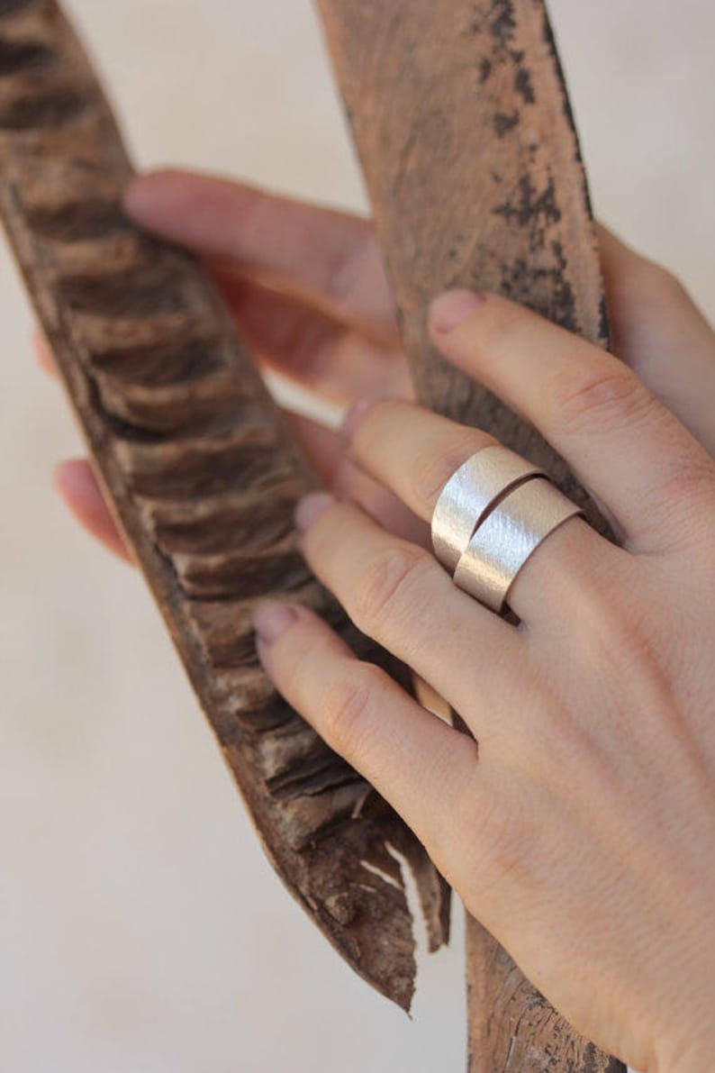 May include: A silver ring with a hammered texture, worn on a finger. The ring is made of two bands that are wrapped around each other.