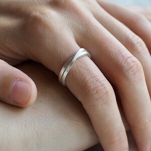 Könnte beinhalten: Ein silberner Ring mit einem gedrehten Design. Der Ring wird an einem Finger getragen.