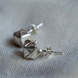 Könnte beinhalten: Ein Paar silberne geometrische Ohrstecker mit einem gefalteten Papierdesign. Die Ohrringe haben einen Stift und einen Schmetterlingsverschluss.
