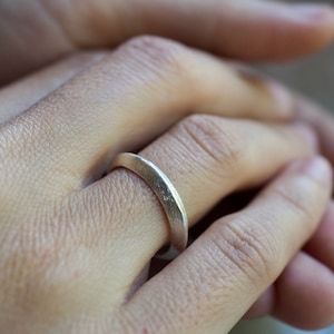 Puede incluir: Un anillo de plata con textura martillada, usado en un dedo.