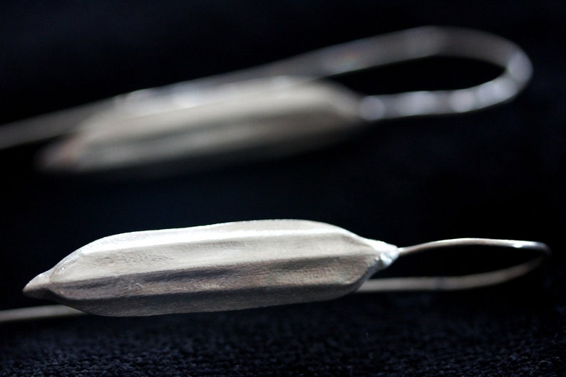 May include: A pair of silver earrings with a textured, elongated, pod-like shape. The earrings have a simple wire hook closure.