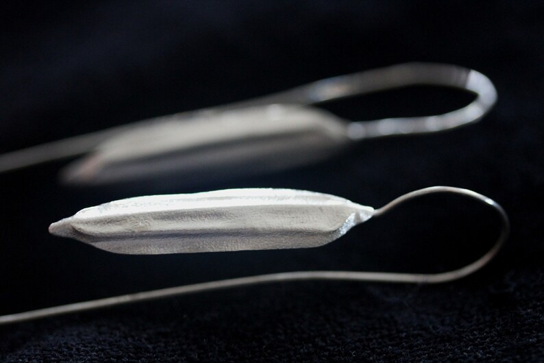 May include: Two silver earrings with a long, thin, curved shape and a textured, elongated, oval-shaped pendant.