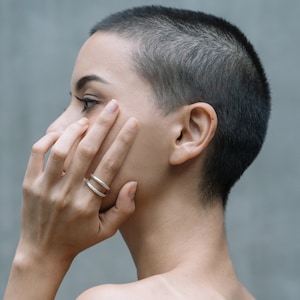 Könnte beinhalten: Eine Person mit kurzen, dunklen Haaren trägt zwei silberne Ringe an ihrem Finger. Die Ringe sind schlicht und elegant, mit einem minimalistischen Design.