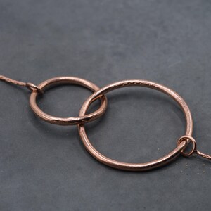 Può includere: Una collana in oro rosa con due cerchi intrecciati. I cerchi sono lisci e hanno una texture leggermente martellata.