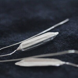 May include: A pair of silver earrings with a long, thin, curved wire and a small, silver, elongated teardrop-shaped pendant.