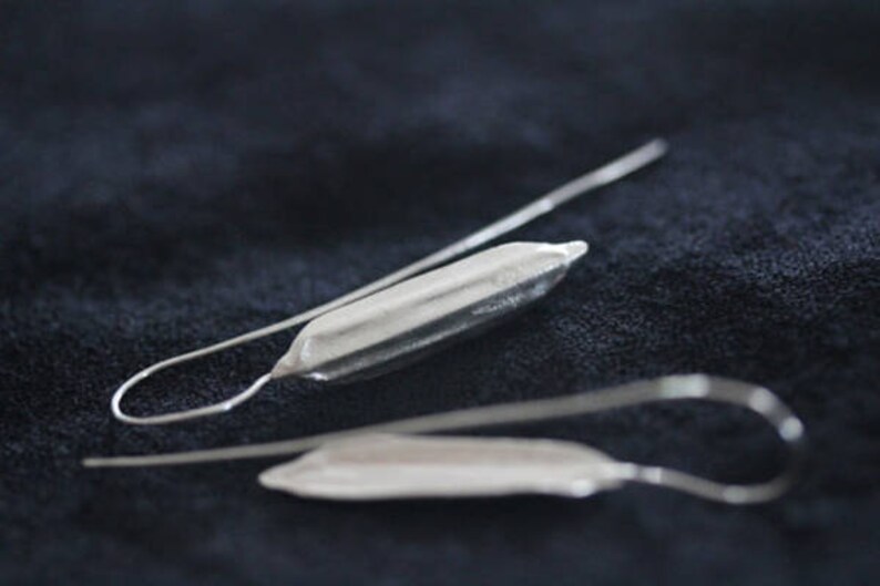 May include: A pair of silver earrings with a long, thin, curved wire and a small, silver, elongated teardrop-shaped pendant.