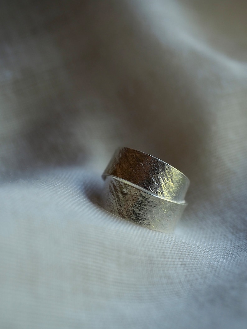 May include: A silver ring with a textured, hammered finish. The ring is designed to be worn on the finger with the band wrapping around twice.