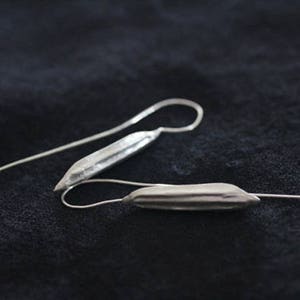 May include: A pair of silver dangle earrings with a long, thin, and slightly curved design. The earrings have a textured, ridged surface.