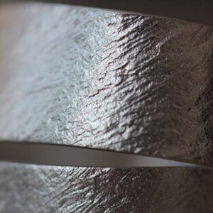 May include: Close-up of a silver metal band with a textured surface. The band is curved and has a subtle sheen.