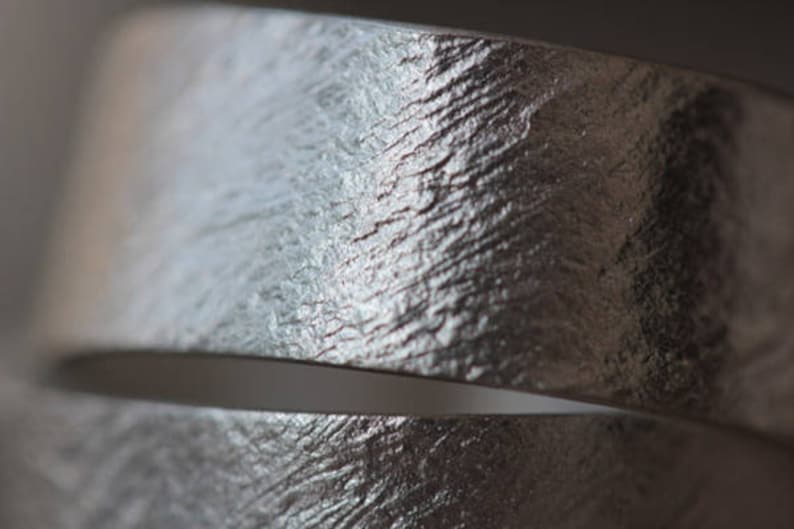 May include: Close-up of a silver metal band with a textured surface. The band is curved and has a subtle sheen.