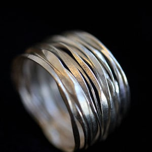 Puede incluir: Un anillo de plata hecho de múltiples bandas delgadas, cada una con una textura martillada, creando un aspecto único y texturizado.