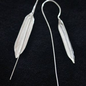 May include: A pair of silver earrings with a long, thin, straight wire and a small, flat, teardrop-shaped pendant.