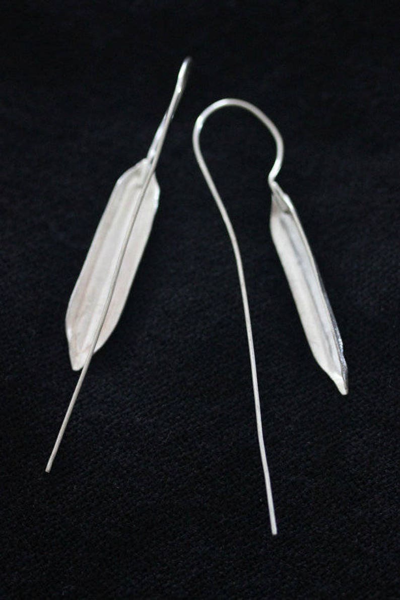 May include: A pair of silver earrings with a long, thin, straight wire and a small, flat, teardrop-shaped pendant.