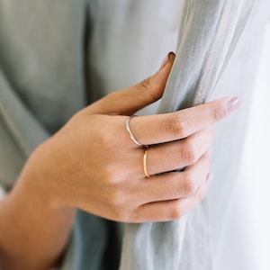 Puede incluir: Una mano con dos anillos finos, uno dorado y otro plateado. La mano está sosteniendo una tela azul claro.