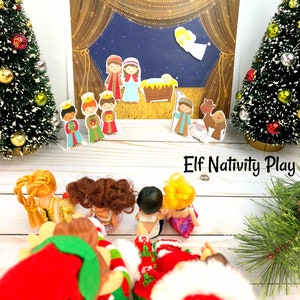 Puede incluir: Un juego de pesebre navideño con personajes de papel de colores, incluyendo a María, José, el niño Jesús y un camello. El set está siendo utilizado por un grupo de elfos vestidos con atuendos navideños rojos y verdes. El texto "Elf Nativity Play" es visible en la parte inferior de la imagen.