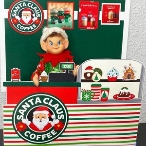 May include: A Christmas-themed coffee shop with a red and green striped counter. The shop is decorated with a Santa Claus coffee logo, a gingerbread house, and a Christmas elf. The elf is wearing a green sweater and a red hat. The sign above the counter reads "Santa Claus Coffee".