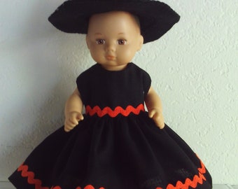May include: A doll dressed in a black witch costume, complete with a pointed hat and a dress with orange trim. The doll has a fair complexion and is posed against a plain white background. The costume is likely for Halloween.