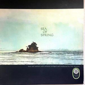 Pode incluir: Capa do álbum com uma serena paisagem marinha com uma ilha e o texto "Sea of Spring". A capa tem uma borda azul escura na parte superior e inferior. O texto "koto and samisen with orchestra arranged and conducted by TAK SHINDO" também está presente.