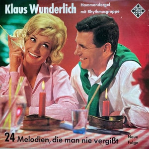 May include: A vintage record album cover featuring a man and a woman sitting at a table with lit candles. The album title is "Klaus Wunderlich" with the text "Hammondorgel mit Rhythmusgruppe" and "24 Melodien, die man nie vergißt" below the image. The album cover is red with a black and white logo in the top right corner.